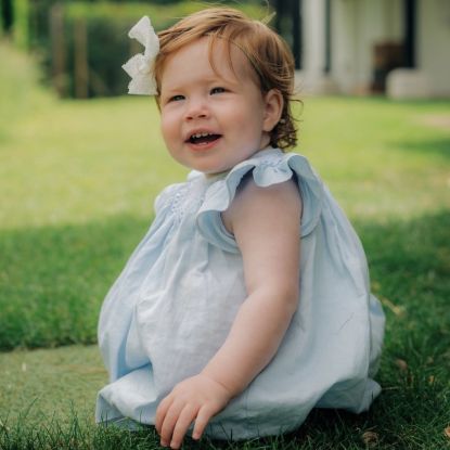 Prince Harry and Meghan Markle's Daughter Lilibet's first birthday portrait sitting in grass smiling in blue dress